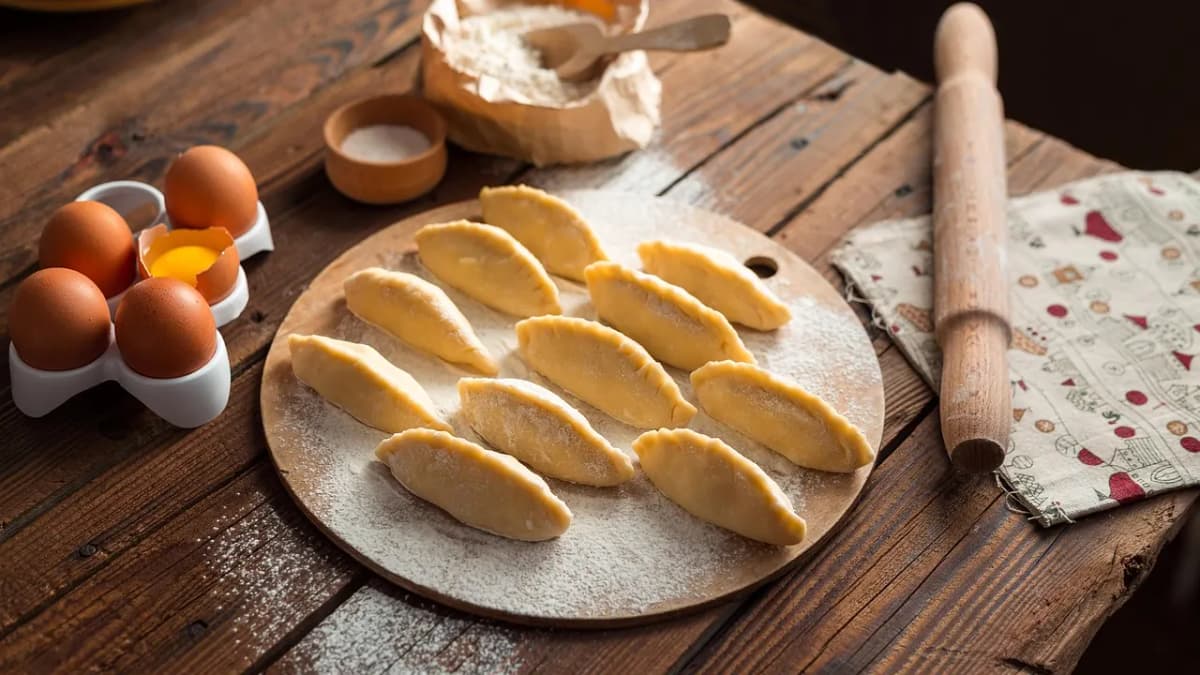 Homemade dumplings on a floured wooden table with eggs and a rolling pin