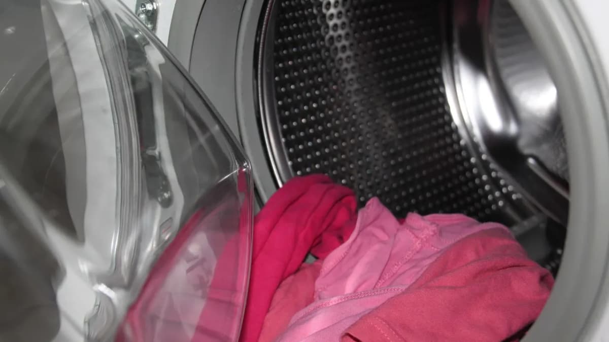 Open washing machine drum with pink clothes inside