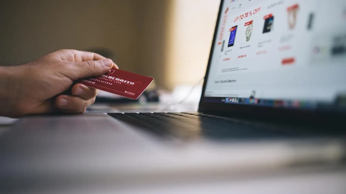 Hand holding a payment card in front of a laptop showing an online shop