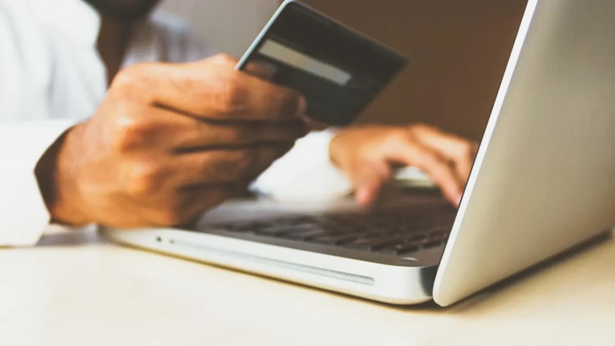 Hand holding a payment card next to an open laptop