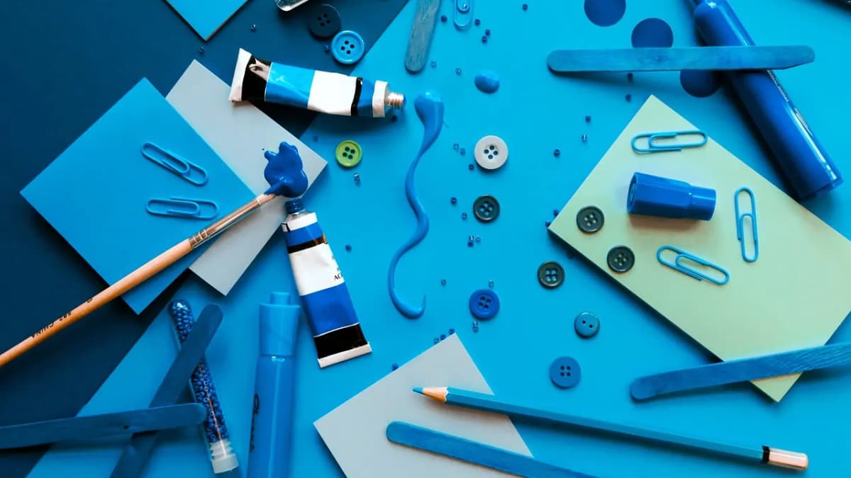 Colourful art supplies, paint tubes and pencils spread on a bright blue desk