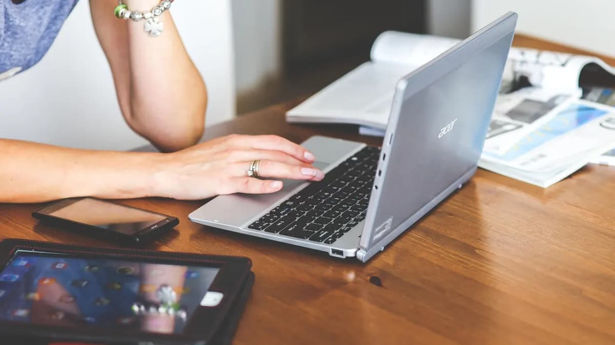 Person working on a laptop with a tablet and smartphone on a wooden desk