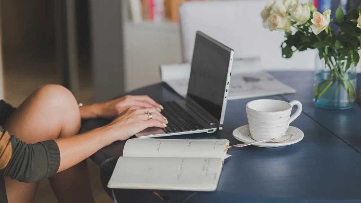 Person writing in a notebook beside a laptop and a cup of coffee