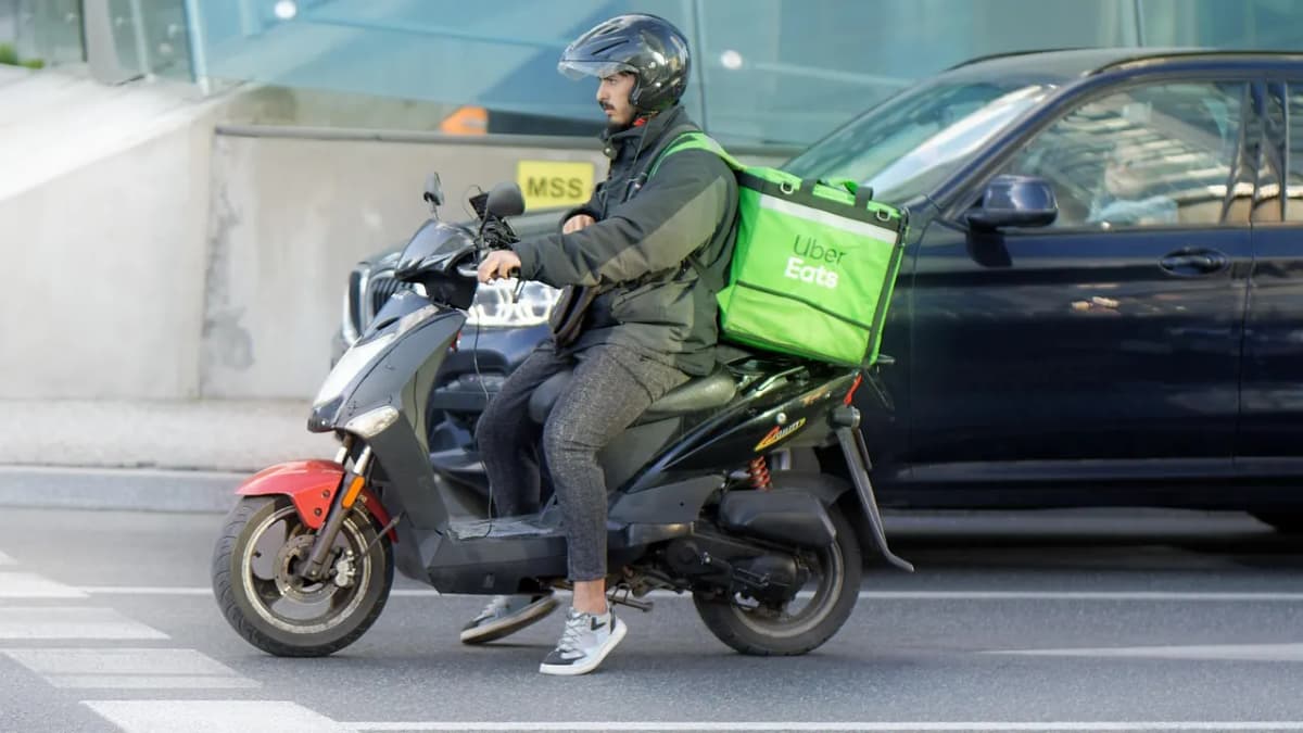 Delivery rider on a scooter with a green food delivery bag riding through the city