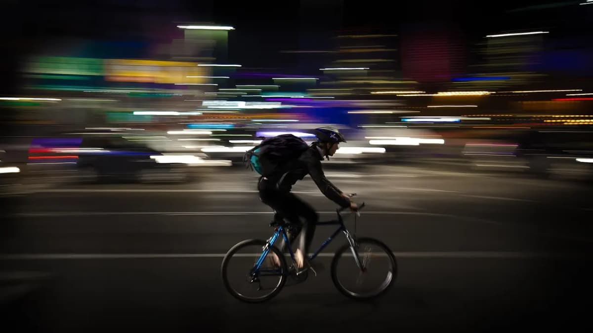 Cyclist courier riding through city traffic at night with light trails