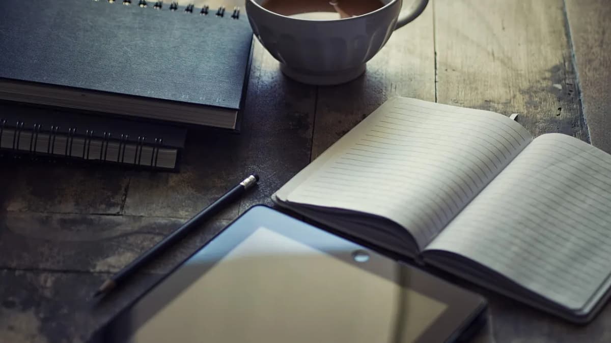 Open notebook, tablet and a cup of tea on a wooden desk