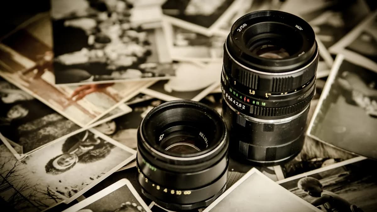 Two camera lenses resting on a pile of printed black and white photographs