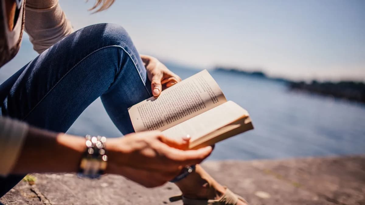 Person reading a paperback book by the sea